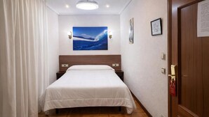 Ein Hotelzimmer mit einem Bett, einer Deckenleuchte, einem Gemälde und einer Tür.