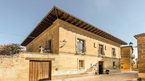 A stone building with a tiled roof, a wooden gate, and a small courtyard. - Hotel Teatrisso (Cuzcurrita de Rio Tiron)