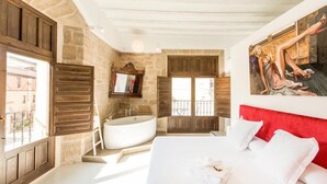 A bedroom with a large bed, a bathtub, and a window with a balcony. - Hotel Teatrisso (Cuzcurrita de Rio Tiron)