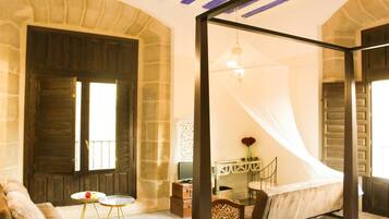 A bedroom with a bed, a desk, and a chair. There is a window with curtains and a mirror on the wall.