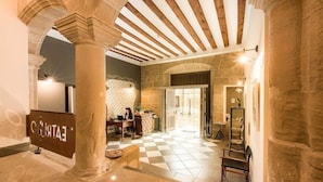 A hotel lobby with stone columns, a checkered floor, a reception desk, and a glass door leading to another area. - Hotel Teatrisso (Cuzcurrita de Rio Tiron)
