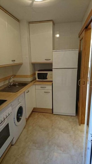 A compact kitchen with a washing machine, a microwave, a sink, and a refrigerator. - Agua/golden Pineda (Salou)