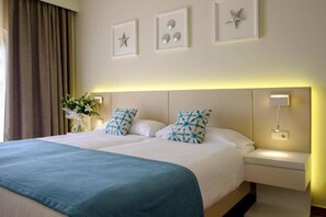 Ein Doppelbett mit blauer Tagesdecke, zwei Kissen mit blauem Muster, ein Nachttisch mit Lampe sowie eine Wand mit gerahmten Bildern und einer Sternverzierung.