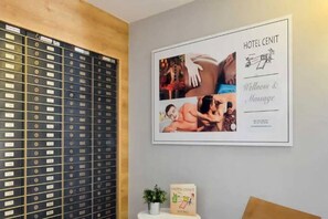 A framed hotel welcome board with wellness & massage services, a wall-mounted filing cabinet, and a small potted plant. - Cenit Apartments (Ibiza Town)