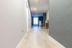 Ein Korridor mit hellem Holzboden, einer grauen Wand rechts und einer Tür am Ende.