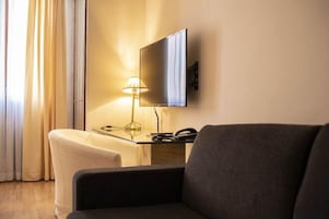 A hotel room with a flat-screen TV mounted on the wall, a desk with a lamp, and a sofa.