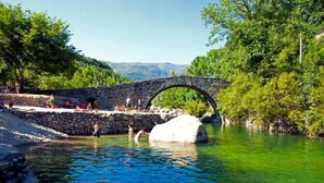 A stone bridge over a river with people swimming and relaxing on the riverbank. - Don Juan de Austria (Jarandilla de la Vera)