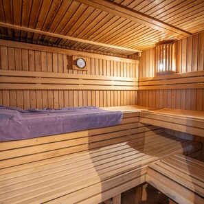 Eine Sauna mit Holzwänden und -bänken, einem sichtbaren Temperaturanzeiger und einem Fenster für natürliches Licht.