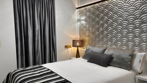 Una cama bien hecha con un edredón a rayas, una pared con un diseño texturizado y una lámpara en una mesita de noche.