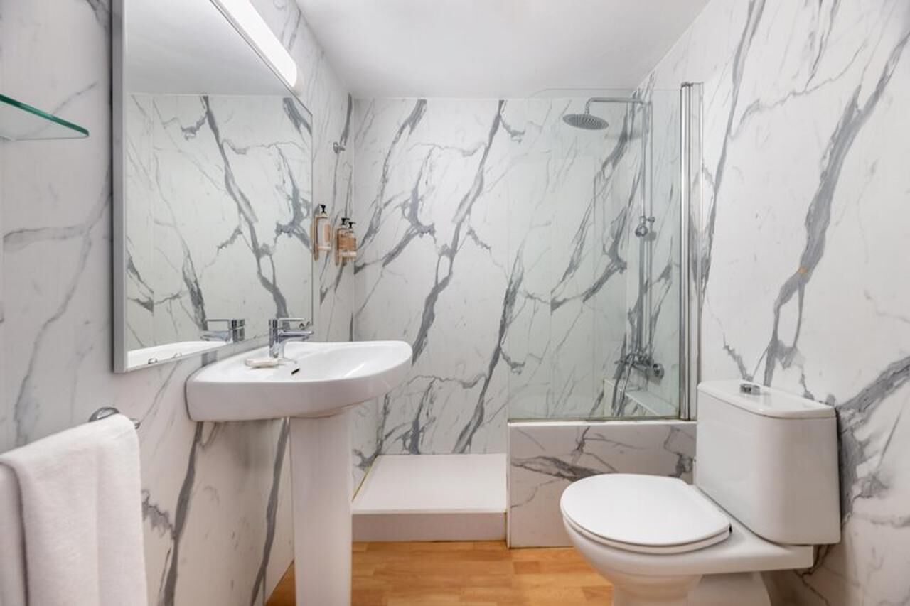 Une salle de bain avec un mur en marbre, un lavabo, des toilettes et une douche.