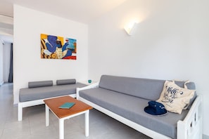 A modern living room with a grey sofa, a wooden coffee table, and a colorful abstract painting on the wall. - Apartamentos Vibra Caleta Playa (Ciutadella de Menorca)