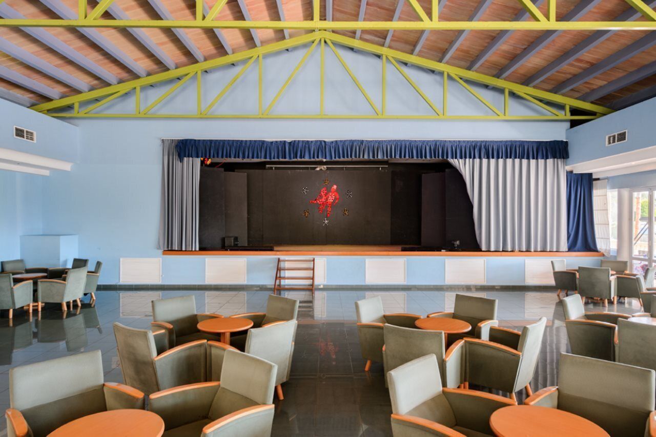 A spacious indoor area with a stage, seating, and a high ceiling with yellow beams.