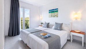 A double bed room with two bedside tables, a window with curtains, a painting on the wall, and a view of the outdoors. - Apartamentos Vibra Caleta Playa (Ciutadella de Menorca)