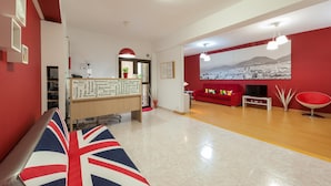 A reception area with a red and white color scheme, a reception desk, a large cityscape mural, a red sofa, and a red chair. - Hotel Las Palmas Urban Center (Las Palmas de Gran Canaria)