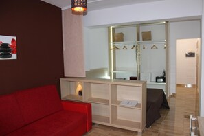 Quarto moderno com sofá vermelho, um armário de madeira e uma cama com cobertura escura.