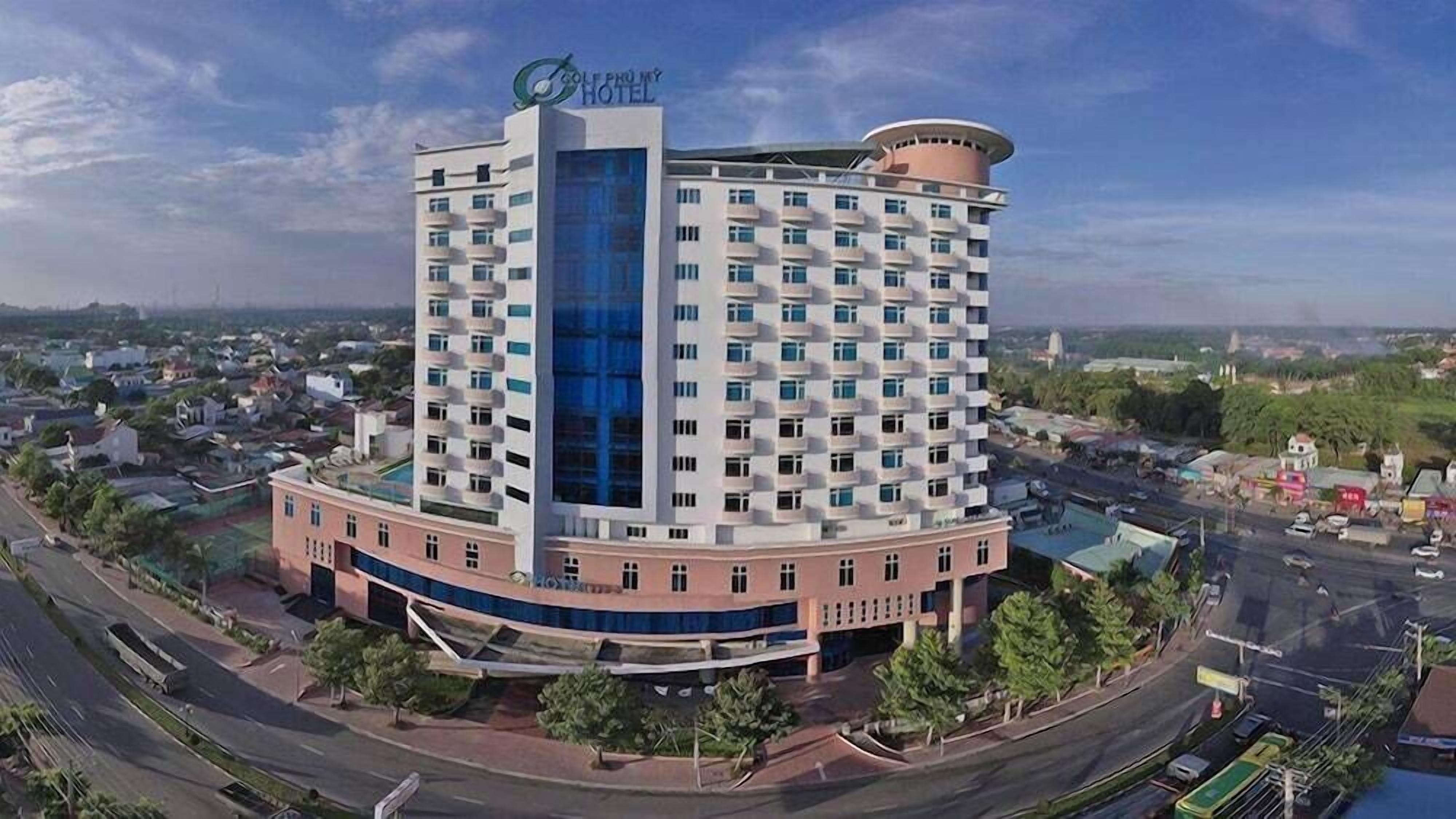 A multi-story hotel with a prominent blue glass facade, surrounded by a landscaped area with trees and a curved driveway.