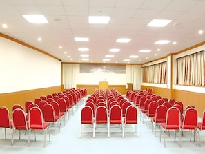 A conference room with rows of red chairs, a podium, and a large window with curtains.