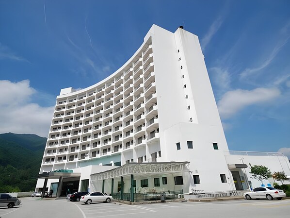 A multi-story hotel with a curved facade, a covered entrance, and a parking area with cars. - Il Sung Jirisan Resort (Namwon)