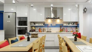 Una cocina moderna con armarios blancos, un refrigerador de acero inoxidable y un comedor con sillas y mesa de madera.