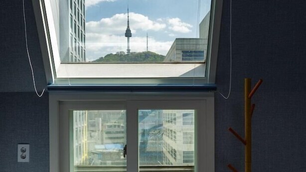 Un dormitorio con tragaluz, cama, perchero y vistas a un paisaje urbano que incluye una torre.
