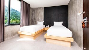 A modern hotel room with two beds, a large window with curtains, a view of greenery, and a dark accent wall. - B2 Phuket (Ratsada)