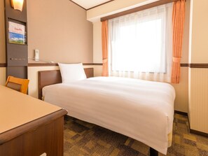 Une chambre d’hôtel comprenant un lit, un bureau, une chaise, une fenêtre avec des rideaux et une lampe fixée au mur.