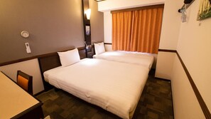 Habitación de hotel con dos camas, un escritorio, una silla, una ventana con cortinas y un termostato fijado a la pared.