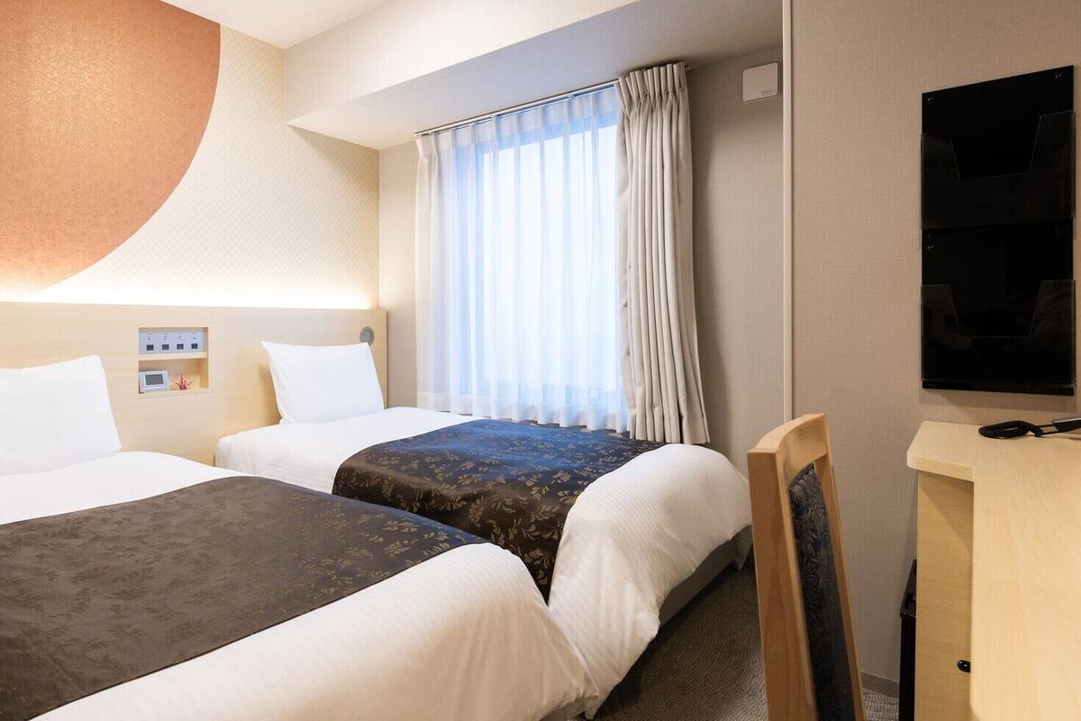 Une chambre d’hôtel avec deux lits, une télévision, un bureau et une fenêtre avec des rideaux.