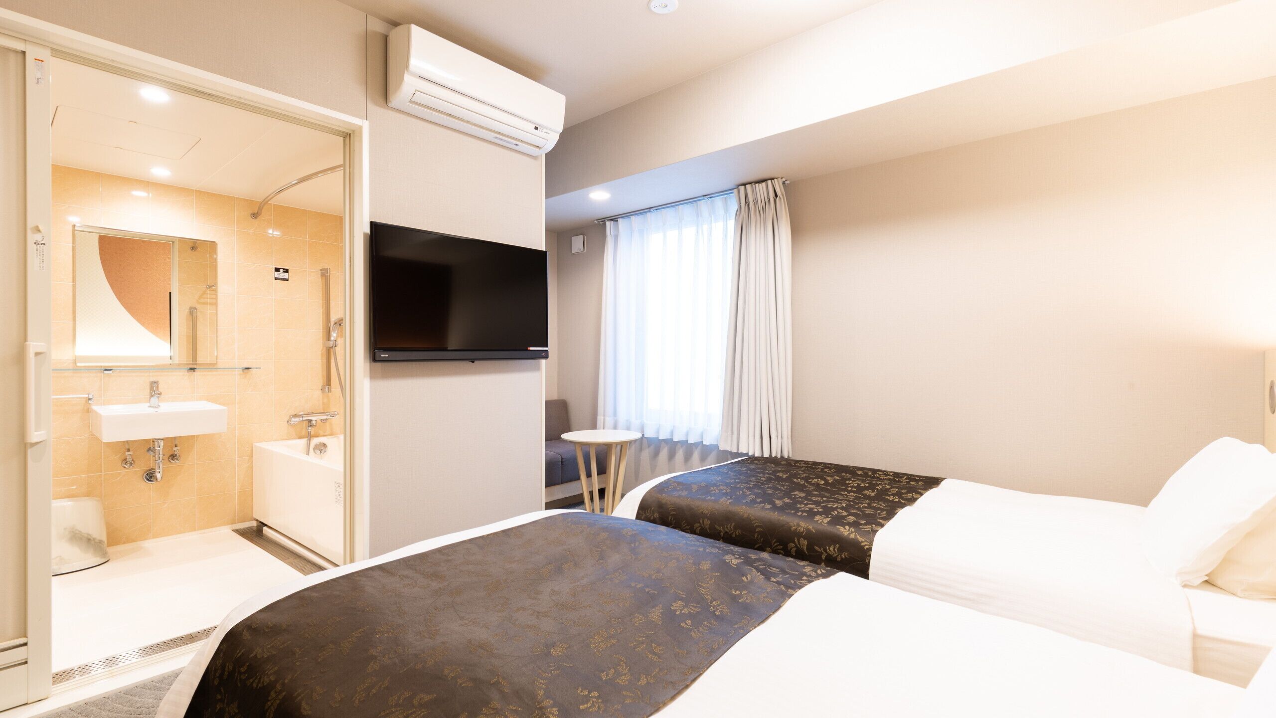 Une chambre d’hôtel comprenant un lit, une télévision, une salle de bain avec un lavabo et une douche, ainsi qu’une fenêtre avec des rideaux.