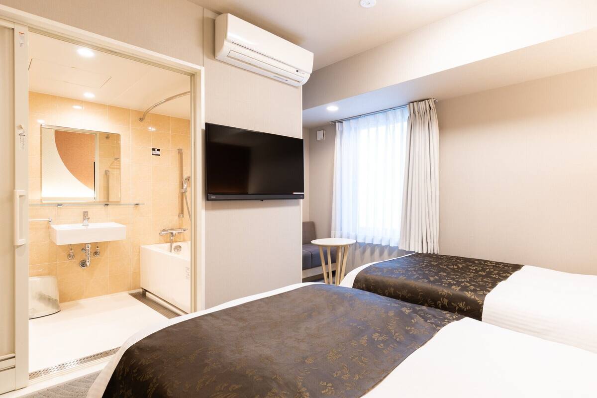Une chambre d’hôtel comprenant un lit, une télévision, une salle de bain avec un lavabo et une douche, ainsi qu’une fenêtre avec des rideaux.
