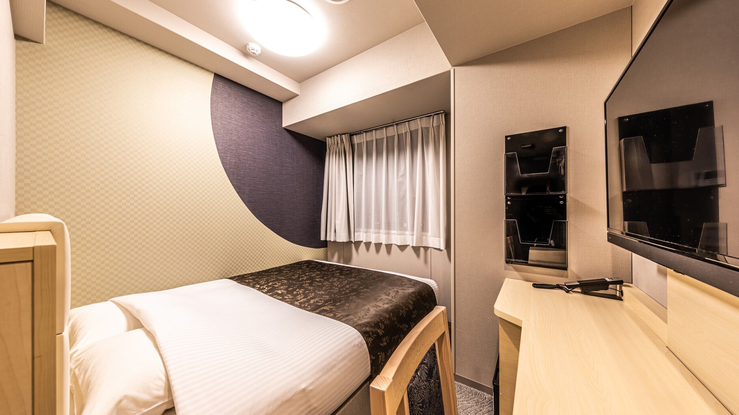 Ein kleines Schlafzimmer mit Bett, Schreibtisch, Stuhl, Fernseher und einem Fenster mit Vorhängen.