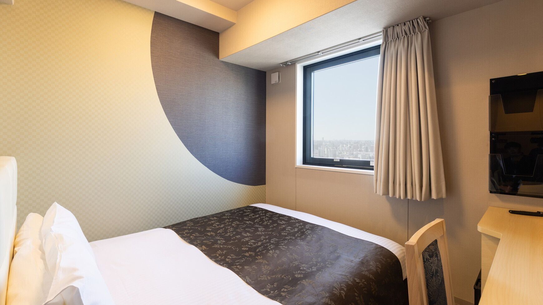 Une chambre d’hôtel avec un lit, un bureau, une chaise, une fenêtre avec des rideaux et une vue sur la ville.