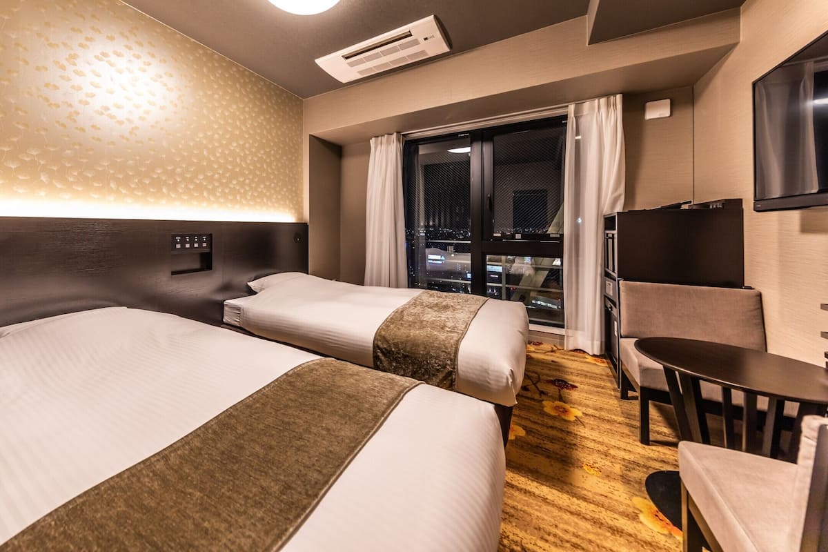 Une chambre d’hôtel avec deux lits, un bureau, une chaise, une télévision et une fenêtre donnant sur la ville.