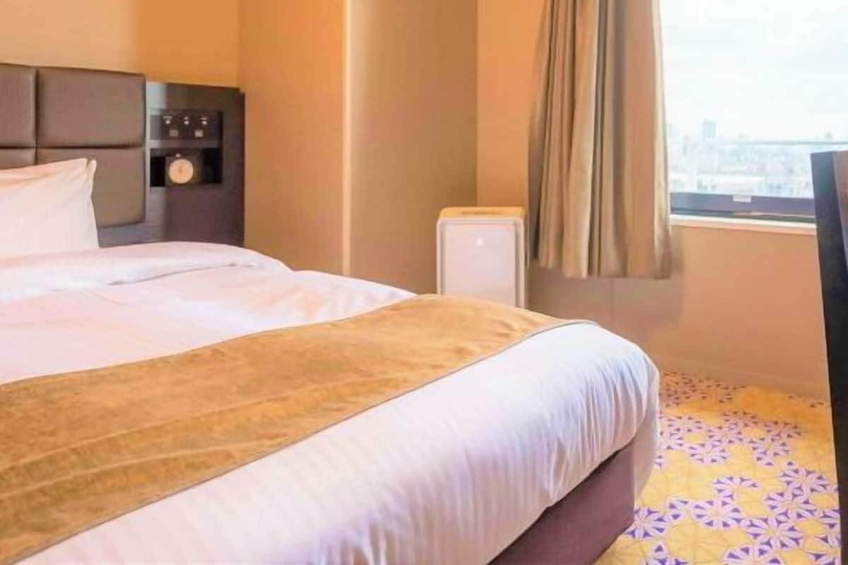 Une chambre d’hôtel avec un lit, une table de chevet, une horloge, une fenêtre avec des rideaux et une vue sur la ville.