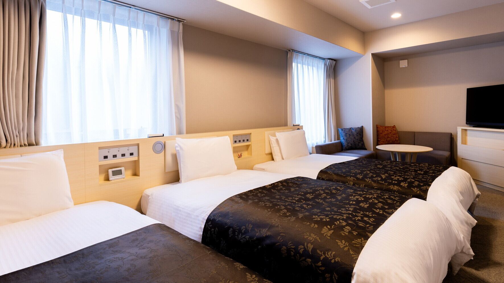 Une chambre d’hôtel avec trois lits, une télévision, une petite table et un canapé.