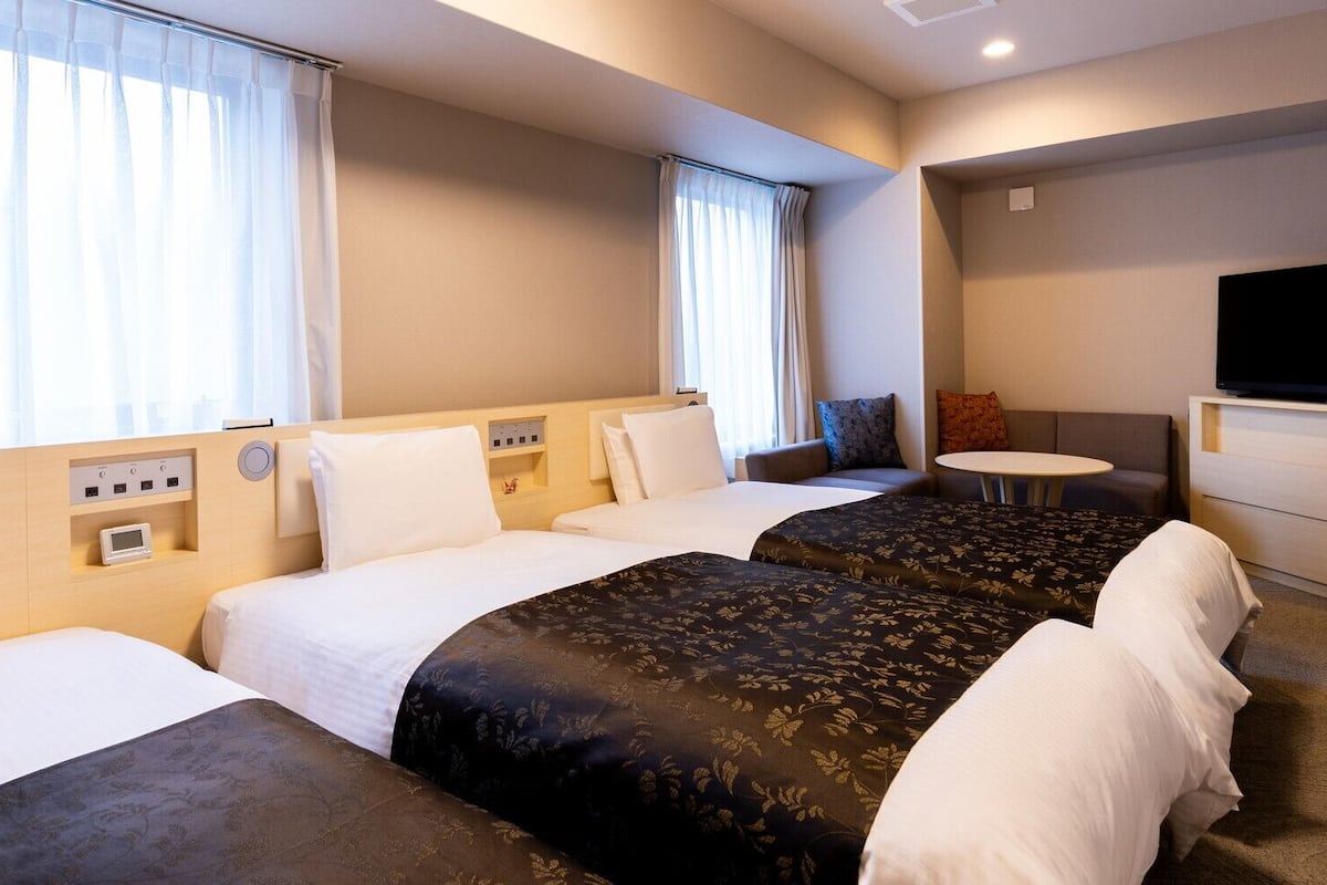 Une chambre d’hôtel avec trois lits, une télévision, une petite table et un canapé.