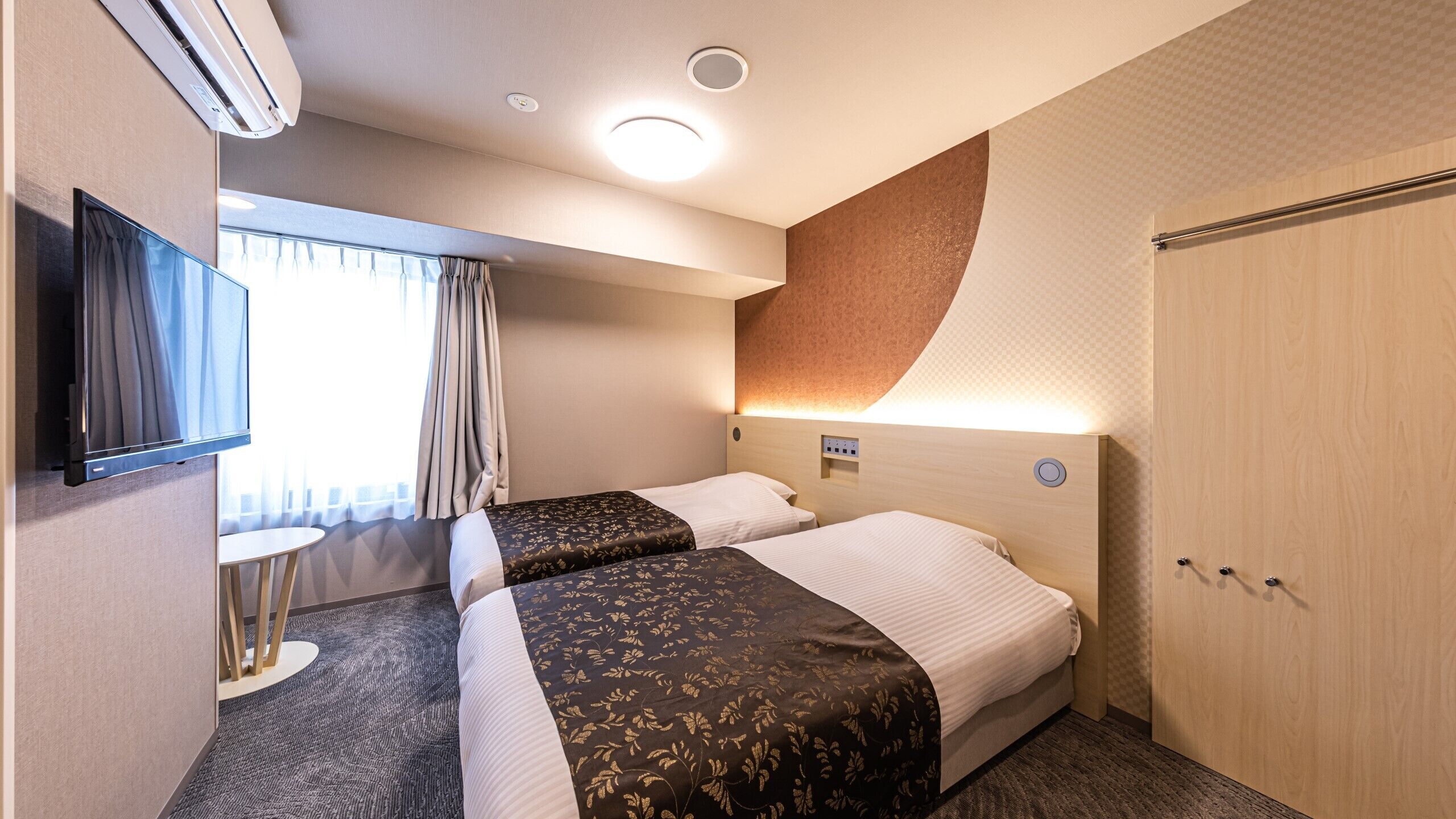 Ein Hotelzimmer mit zwei Betten, einem Fernseher, einer Klimaanlage, einem kleinen Tisch und einem Kleiderschrank.