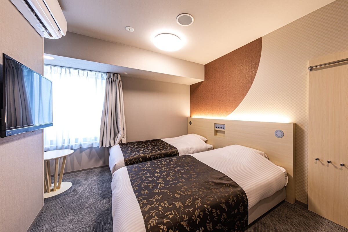 Une chambre d’hôtel avec deux lits, une télévision, la climatisation, une petite table et une armoire.