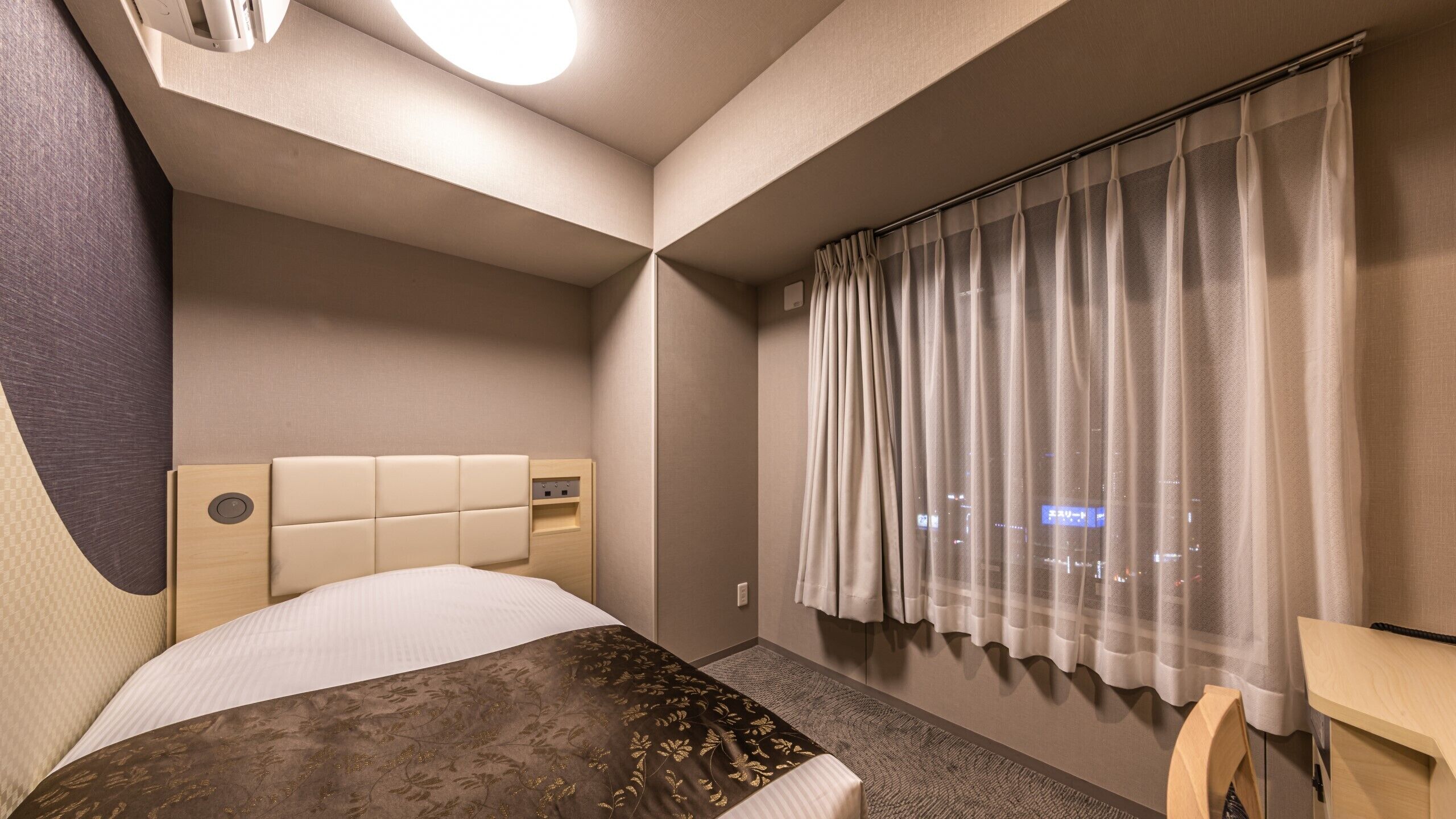 Ein Hotelzimmer mit Bett, Schreibtisch, einem Fenster mit Vorhängen und Blick auf die Stadt.