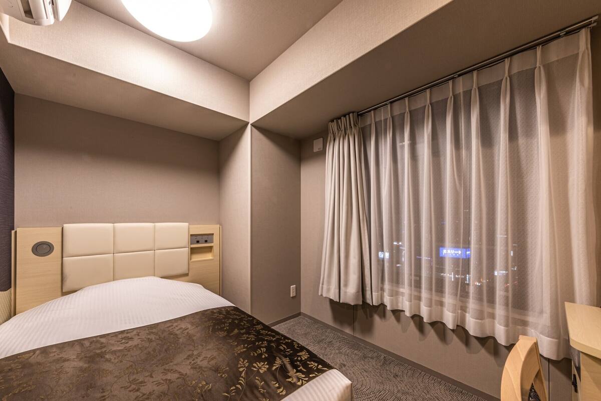 Une chambre d’hôtel avec un lit, un bureau, une fenêtre avec des rideaux et une vue sur la ville.