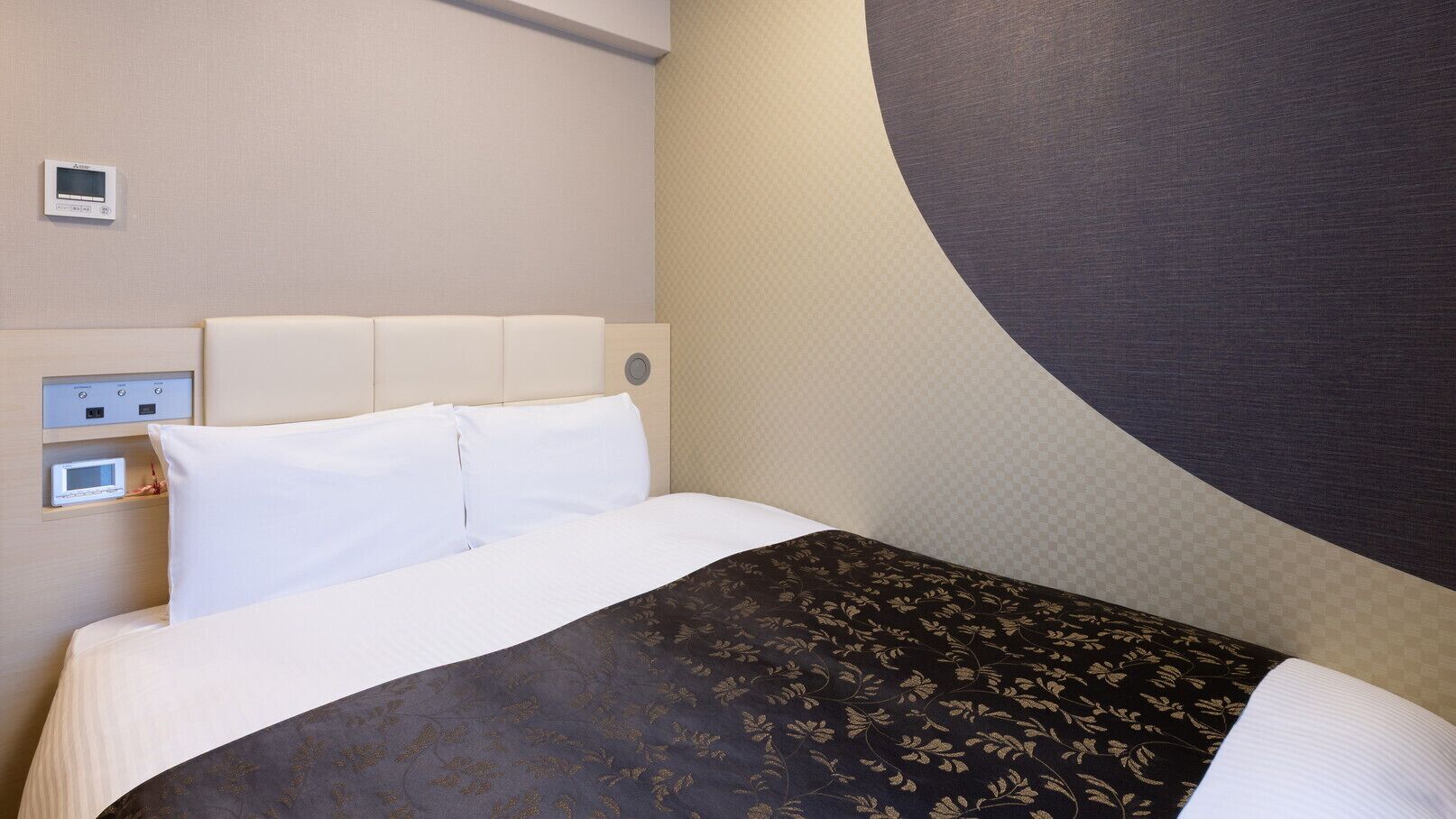 Une chambre d’hôtel avec un lit, un panneau de commande et une grande horloge murale.