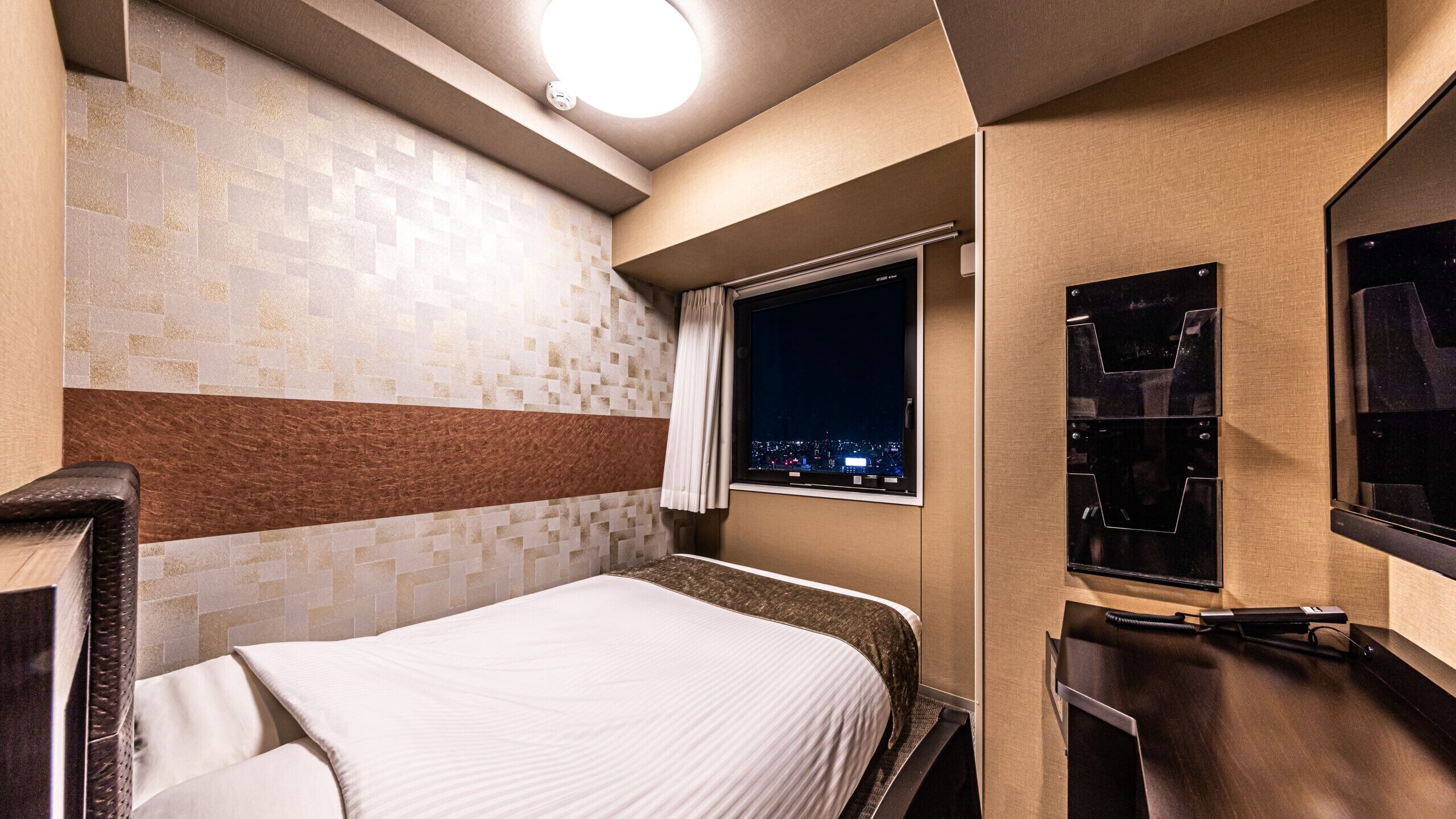 Ein Hotelzimmer mit Bett, Fenster mit Stadtblick, Spiegel und einem an der Wand befestigten Fernseher.