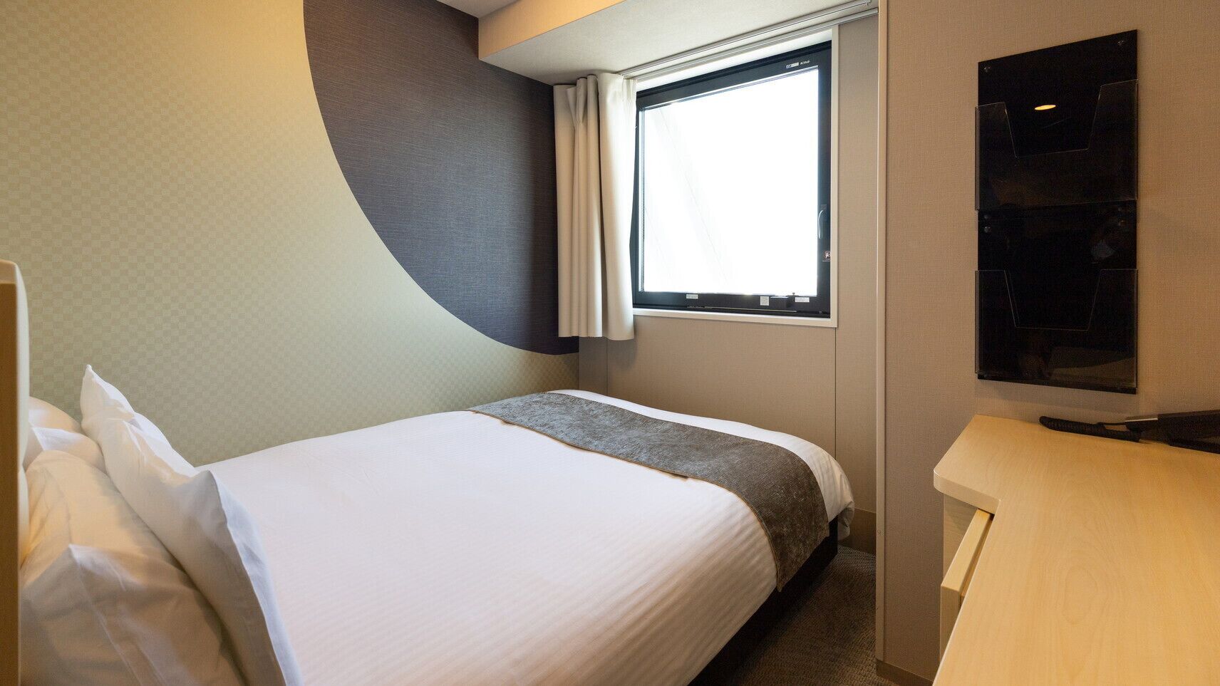 Une chambre d’hôtel avec un lit, une fenêtre, un téléviseur à écran plat et un bureau en bois.