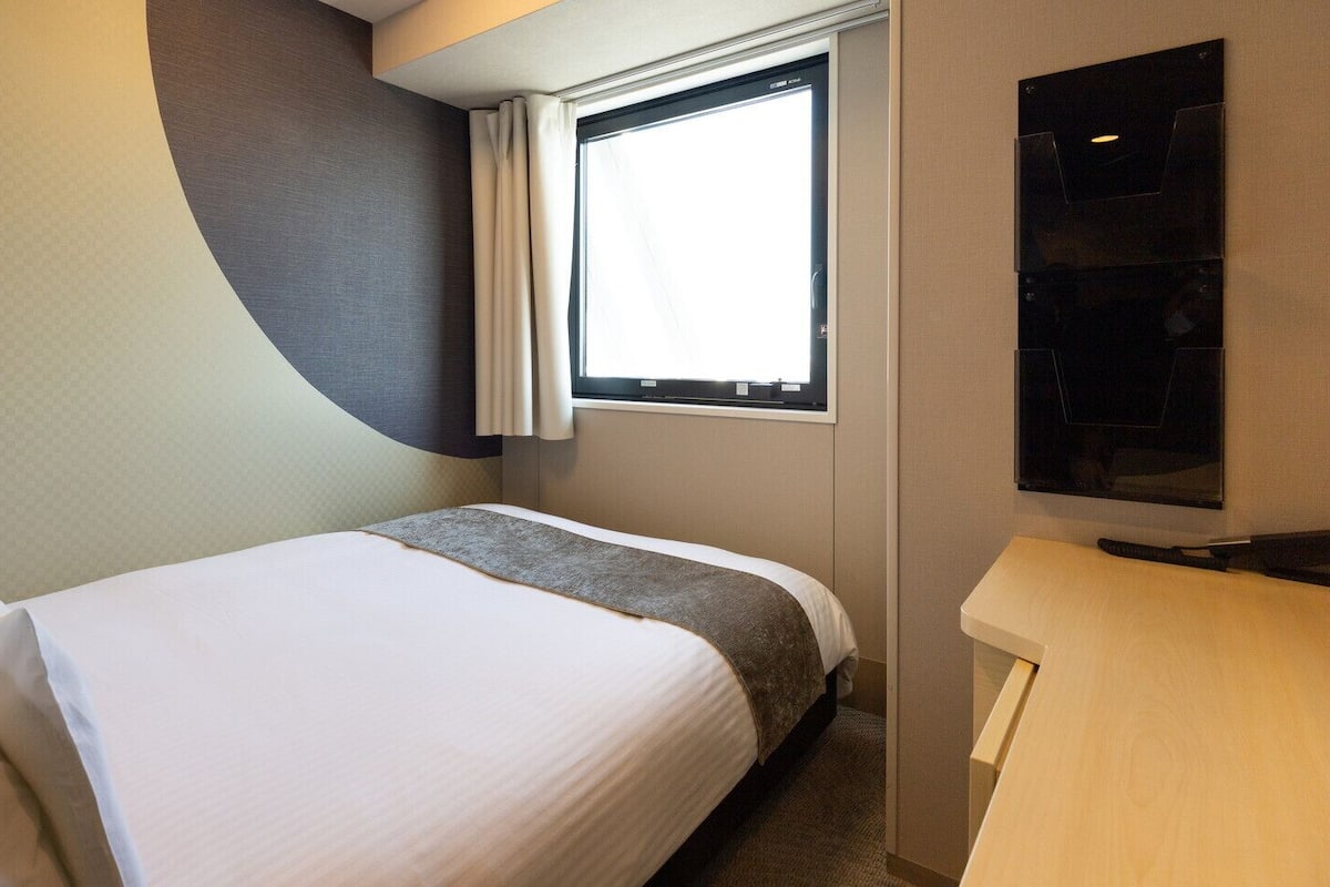 Une chambre d’hôtel avec un lit, une fenêtre, un téléviseur à écran plat et un bureau en bois.