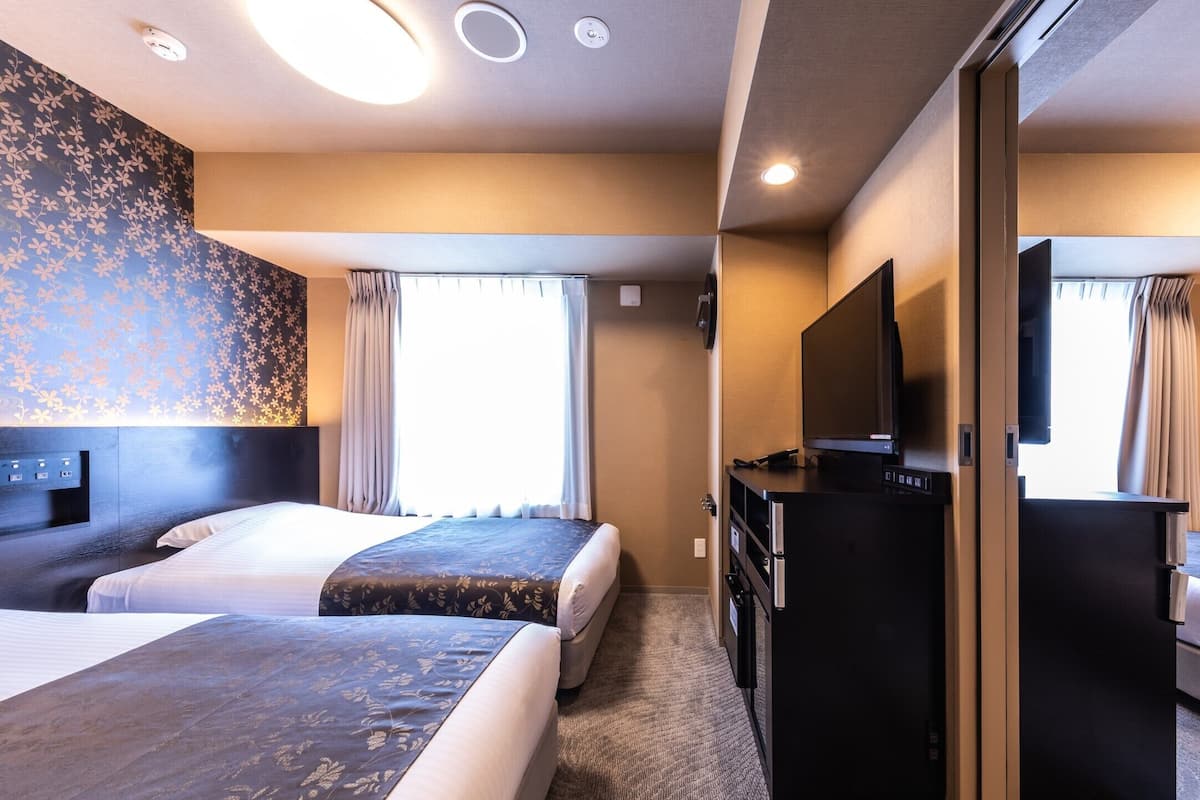 Une chambre d’hôtel avec deux lits, un bureau, une télévision et un miroir.