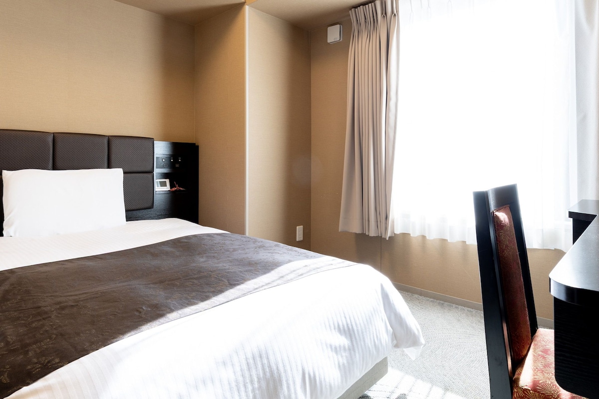 Ett hotellrum med en säng, ett skrivbord och en stol.
