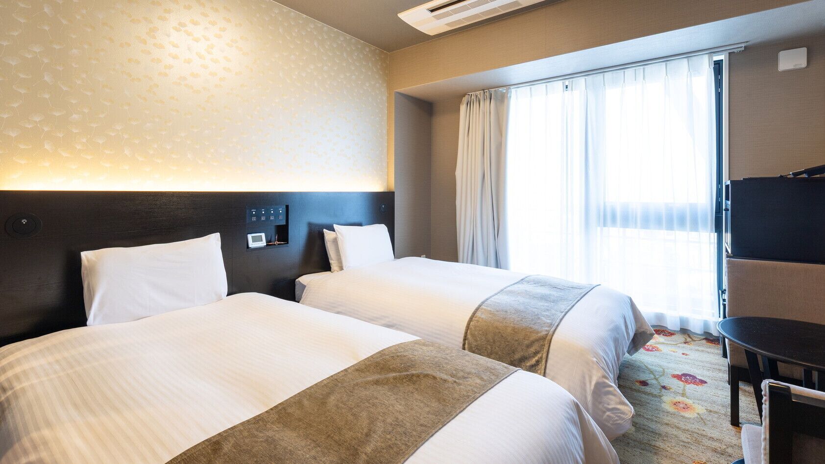 Une chambre d’hôtel avec deux lits, un bureau, une chaise, une télévision et une fenêtre avec des rideaux.