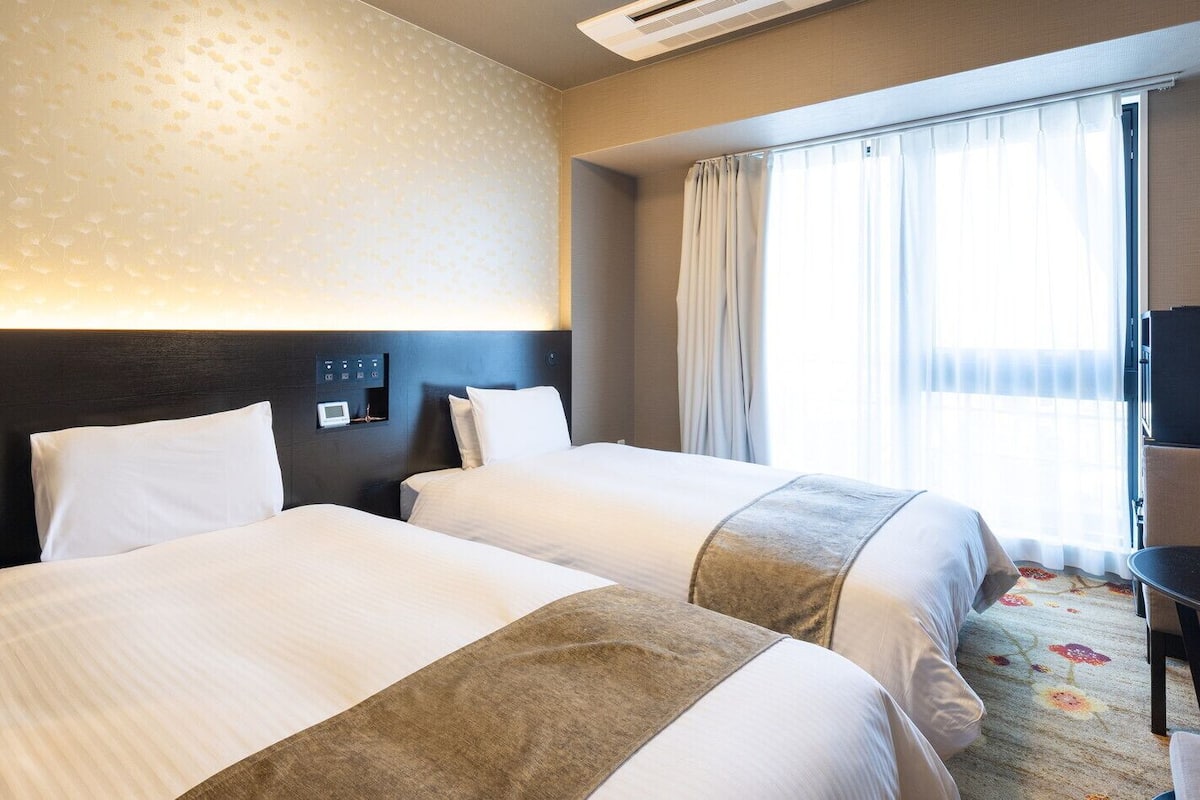 Une chambre d’hôtel avec deux lits, un bureau, une chaise, une télévision et une fenêtre avec des rideaux.