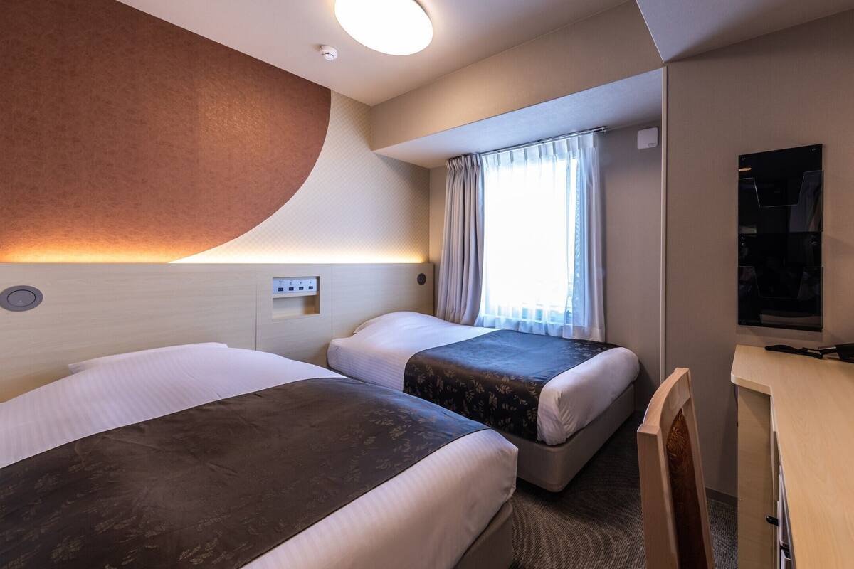 Une chambre d’hôtel avec deux lits, un bureau, une télévision et une fenêtre avec des rideaux.