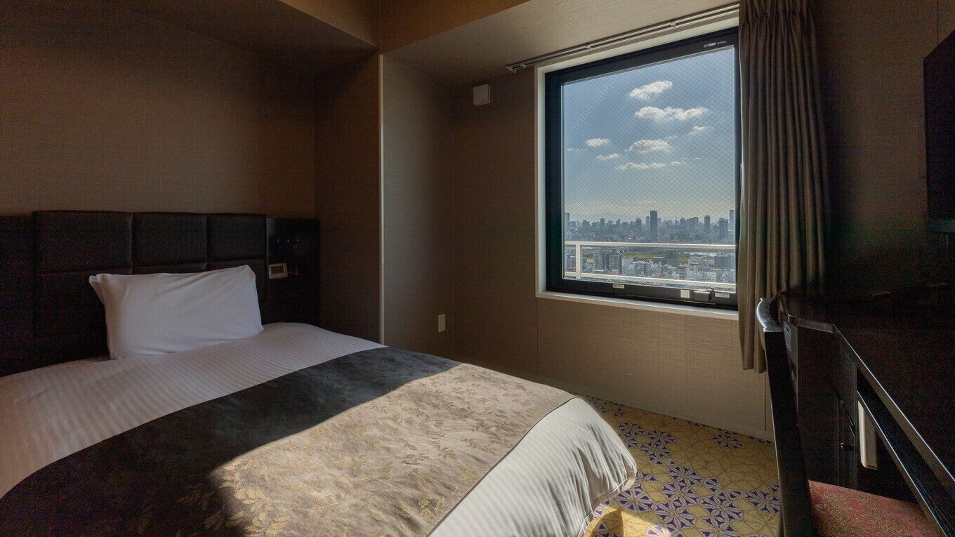 Une chambre d’hôtel avec un lit, une fenêtre donnant sur la ville et une porte.